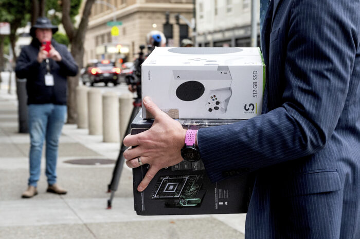 A legal worker carries Xbox boxes into the Phillip Burton Federal Building and U.S. Courthouse on Wednesday, June 28, 2023 in San Fransisco. Microsoft is defending the company's proposed $69 billion takeover of video game maker Activision Blizzard as federal regulators seek to block the deal. (AP Photo/Noah Berger)